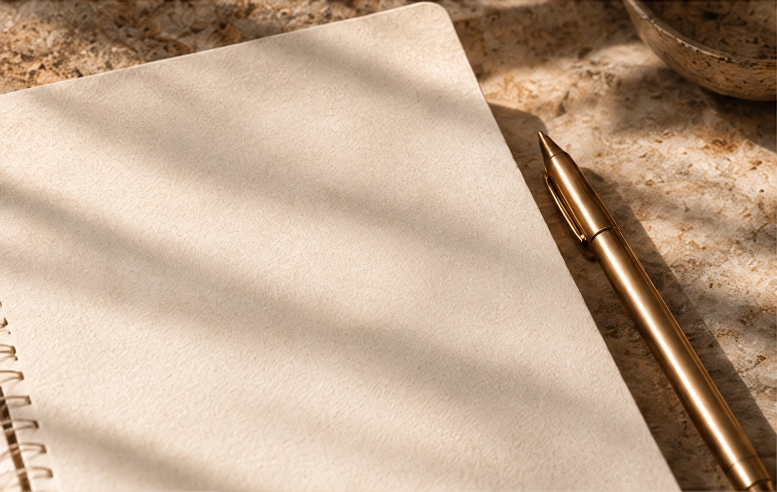 Caderno aberto, sem escrita, com encadernação e caneta sobre pedra.